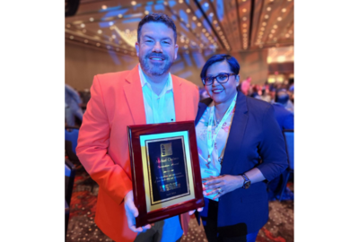 Michael Chalmers, in orange sport coat, holding a plaque, next to Kathy George, in navy blazer, both smiling at the camera